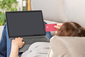 Back view of a woman using her credit card to make an online payment at home
