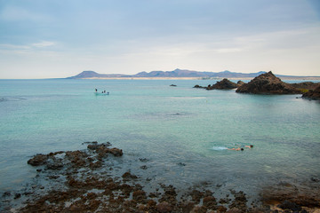 Paisaje azul turquesa marítimo de rocas con pequeño barco y personas haciendo snorkel