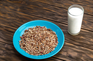 Muesli flakes in blue plate and glass of milk on wooden background