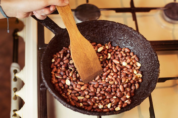Girl fries at home in a frying pan useful peanut. Girl loves to eat fruits and nuts during the day