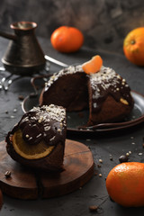 Traditional British steam chocolate pudding with oranges, clementines and coconut shreds served with coffee on wood slab on black background