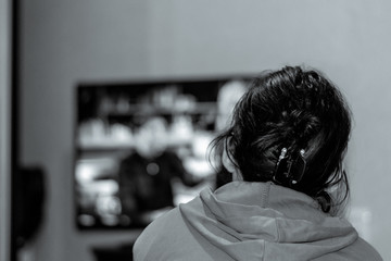 Brunette woman is watching TV. Rear view of a girl watching tv