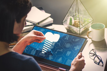 Woman with laptop on her desk. She holds the teeth implant icon. Search for dentists, dental services, consultations.