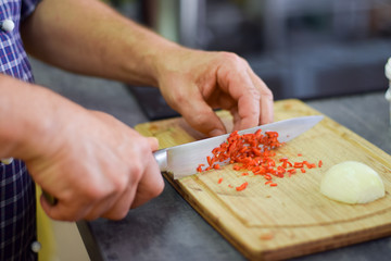 Hands chopping red pepper thinkly on the wooden chopping board