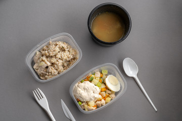 Olivier salad and oatmeal with chicken in plastic container on gray background. Top view.