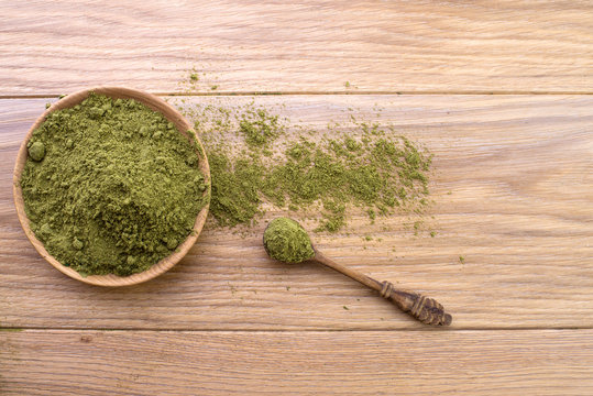 Hemp flour in wooden bowl, powder in spoon, cannabis leaves on the background of the wooden board