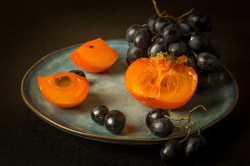 ripe persimmons and black grapes on a plate on a black background