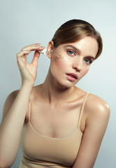 A beautiful young natural girl without makeup applies a serum to a face with a pipette.