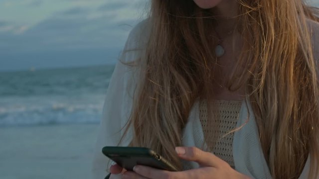 Young woman at the beach using her cellphone by the ocean