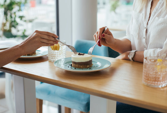 Anonymous young women sharing a cake at coffee shop