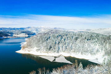 Winter in Croatia. Panorama of Lokvarsko lake and woods under snow in Gorski kotar and Risnjak mountain in background from drone.
