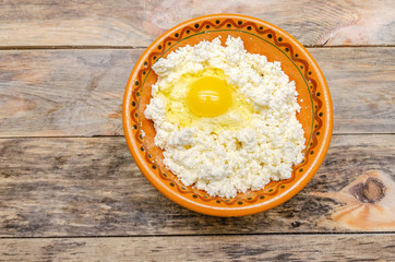 Cottage cheese with a broken egg in a brown bowl, top view