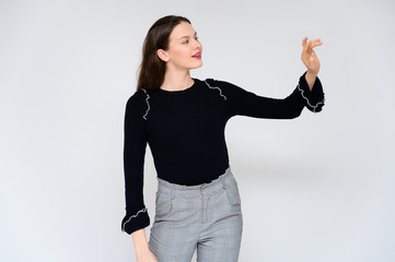 Concept adult girl on a white background. A photo of a pretty brunette girl in gray trousers and a black sweater smiles and shows different emotions in different poses right in front of the camera.