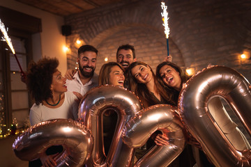 People at New Years party, waving with sparklers and holding 2020 balloons