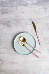 blue empty plates with gold fork, spoon and knife on a grey stone background, flat lay