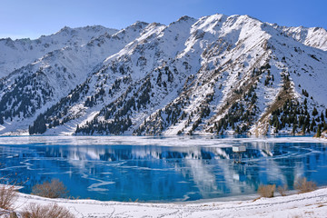 Autumn gives way to winter, air temperature drops and the water in the lake begins to freeze. Texture and patterns of ice on the serene water surface of a mountain lake; Big Almaty lake in Kazakhstan