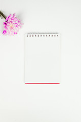Blank notebook with pink flower on a white background. Top view of little plant with flowers on blank notebook on white fabric workspace background. Copyspace, mockup