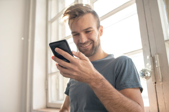 Smiling man using smartphone at the window