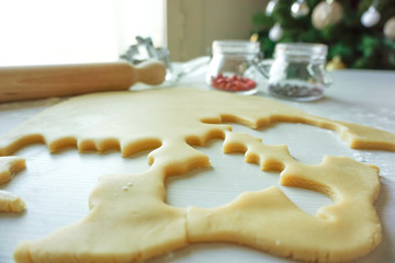 A cookie dough cutted in table with deer festive cutter and jars with decorative chocolate with the christmas tree in background- Homemade biscuits in the kitchen for new year holiday