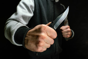 Knife in the hand of a man attacking from the dark, close-up