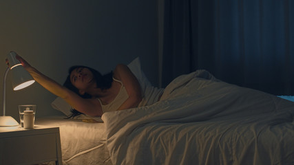 Beautiful Asian young woman sleeping cozily in her bedroom. Indian female hand turning off on light...