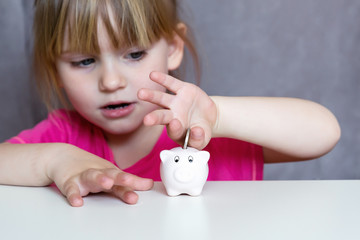 Girl hand inserting a coin into a piggy bank.