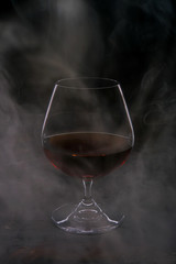 Glass glass with cognac filled with smoke on a dark background.