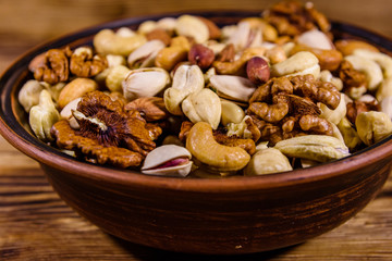 Various nuts (almond, cashew, hazelnut, pistachio, walnut) in ceramic plate on a wooden table. Vegetarian meal. Healthy eating concept
