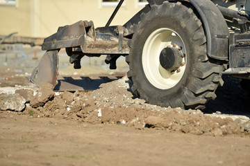 A tractor with a bucket performs construction work on cleaning the territory at a construction site.