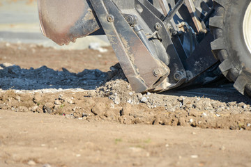 A tractor with a bucket performs construction work on cleaning the territory at a construction site.