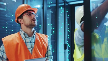 Multi-race team of database technicians working on server racks, fixing tech bugs and problems, running diagnostics on digital tablet, cooperating at server room data center. - Powered by Adobe