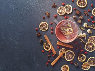 A large mug with a sachet of healthy dried plants is on a dark concrete background. Nearby are various dried herbs and berries (lemon slices, rose hips, anise stars). Making a healthy vitamin drink.