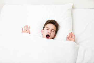 Sleeping child boy lying bed hiding yawning face with blanket