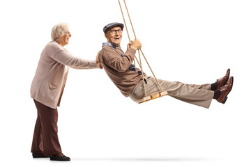 Elderly wife pushing her husband on a swing