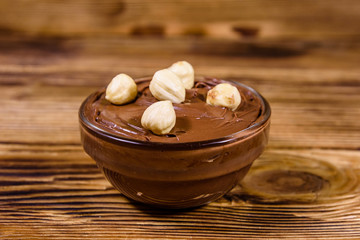 Glass bowl with chocolate spread and hazelnuts on a wooden table