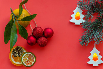 Christmas and New Year composition. Fresh tangerine with green leaves, slices of dried mandarin,  Xmas lights, red balls, cone on a red background. Flat lay,Top view