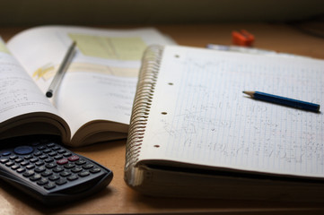 A notebook with math exercises written in pencil next to a calculator
