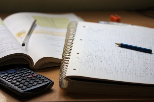 A notebook with math exercises written in pencil next to a calculator