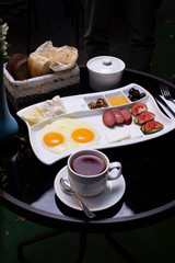 tasty breakfast, tea, bread, honey, egg, sausage, olives, tomato and cucumber on the table