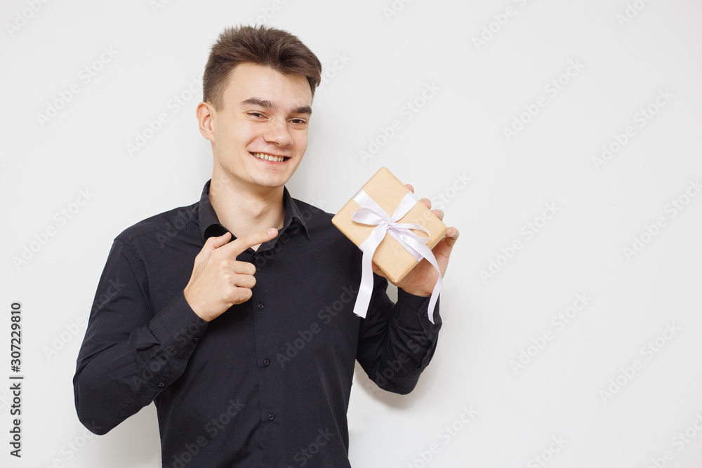 Wall mural Man with a happy face and a gift box, pointing at that. with copy space