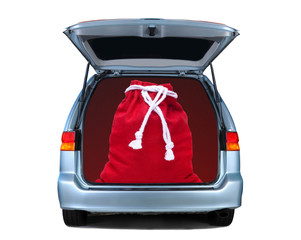 Santa Claus large bag of toys in the back of a Minivan with its rear door open. Square format isolated on white with shadow under vehicle.