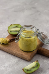 Homemade kiwi jam in a preserving glass. Exotic kiwi jam. Light grey stone background, selective focus.