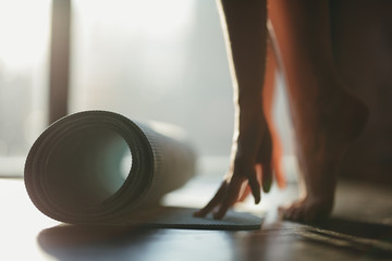 A girl rolls a rug with her hands and stands on toes on the floor for yoga in a fitness studio or at home in sunny weather