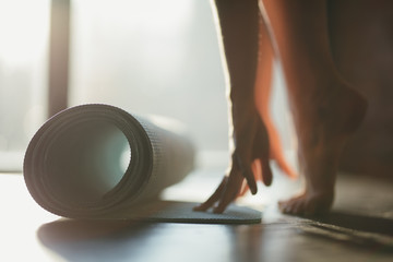 A girl rolls a rug with her hands and stands on toes on the floor for yoga in a fitness studio or at home in sunny weather