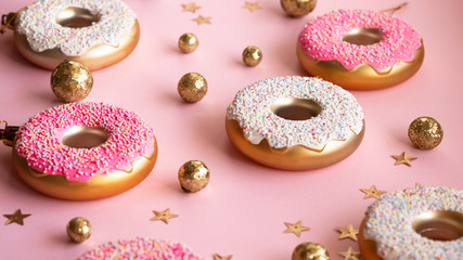 Christmas toys in the form of donuts on a pink background with gold decor, selective focus. Creative food minimalism
