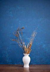 White vase with dry branches on a blue background