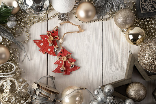 Christmas composition of a wooden star, Christmas gold and silver blinders, wooden heart, branches, gold beads on a white natural wooden background with a red wooden Christmas tree in the center.
