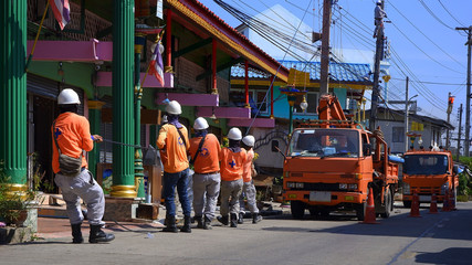 Side view of electricians team with crane trucks on the street are working to installation cable lines on electric power poles at rustic village