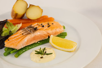 Grilled fresh salmon steak with roasted green beans, baked potatoes, lime and salad vegetables is a healthy diet for dieting on a plate.