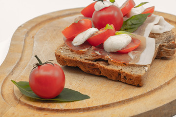 Sandwich italien au couleur du drapeau italien vert blanc rouge avec des tomates cerises du basilic et des billes de mozzarela sur du jambon d'Aoste et une tranche de pain de campagne assiete en bois